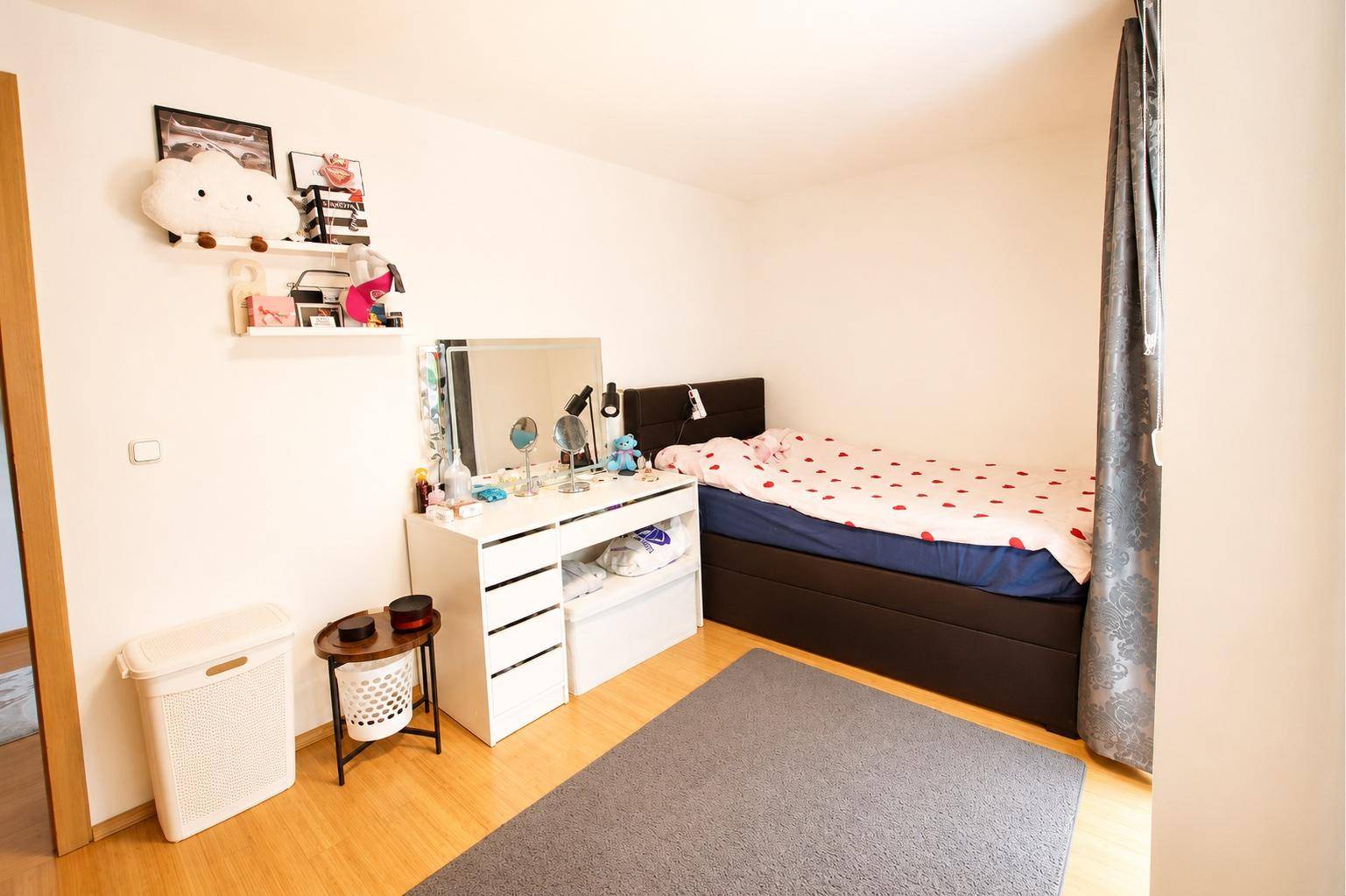 Gemütliches Schlafzimmer mit Holzboden, weißem Schminktisch und dekorativen Wandregalen.