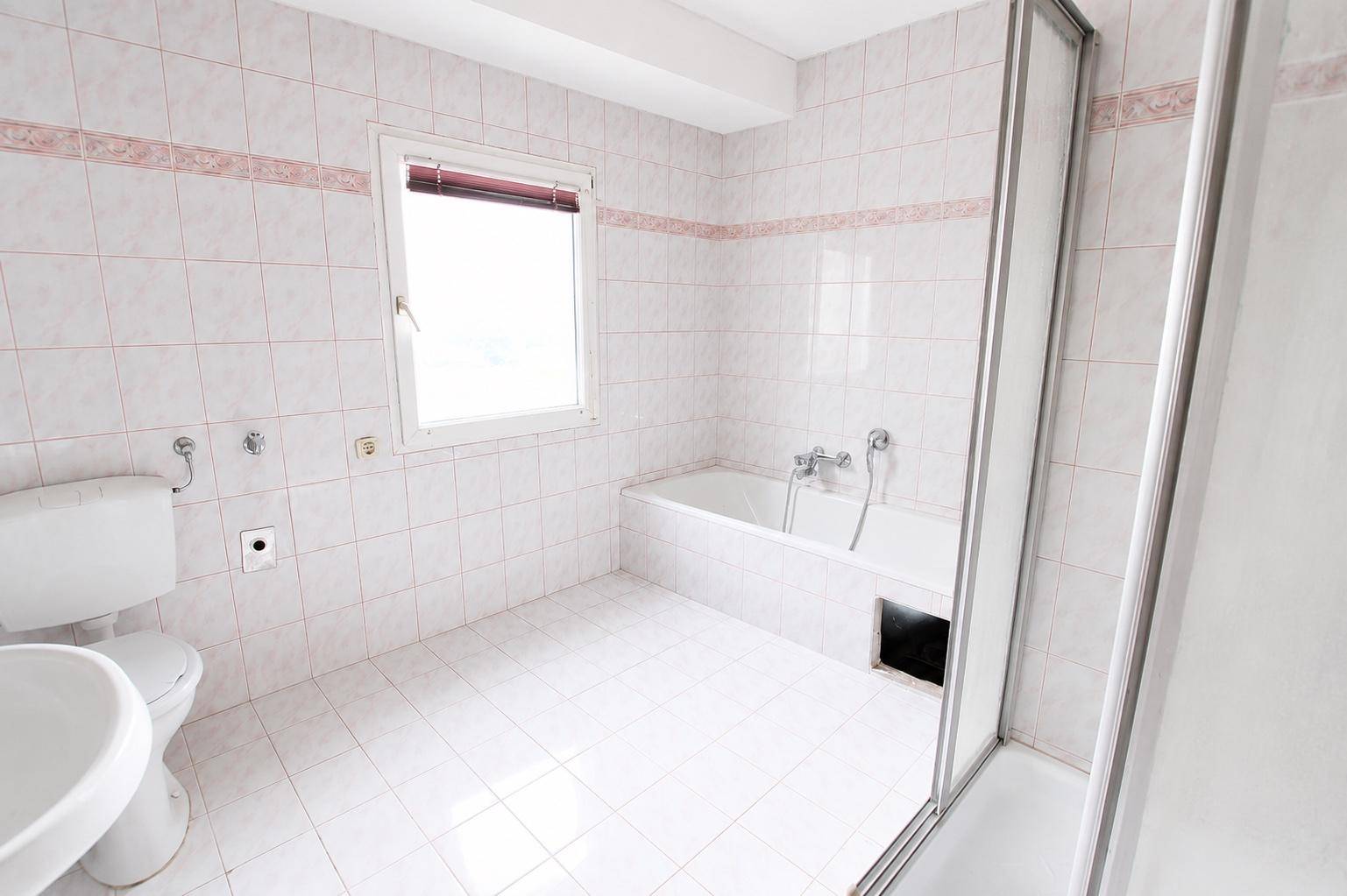Helles Badezimmer mit weißen Fliesen, Badewanne, Dusche und Fenster.