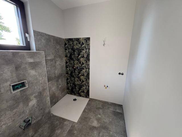 Unfertiges Badezimmer mit begehbarer Dusche, floraler Wandgestaltung und Fenster.