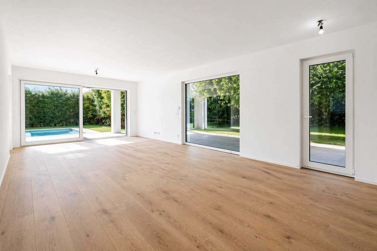 Heller, leerer Wohnraum mit Eichenparkett und großen Fensterfronten zum Poolbereich.