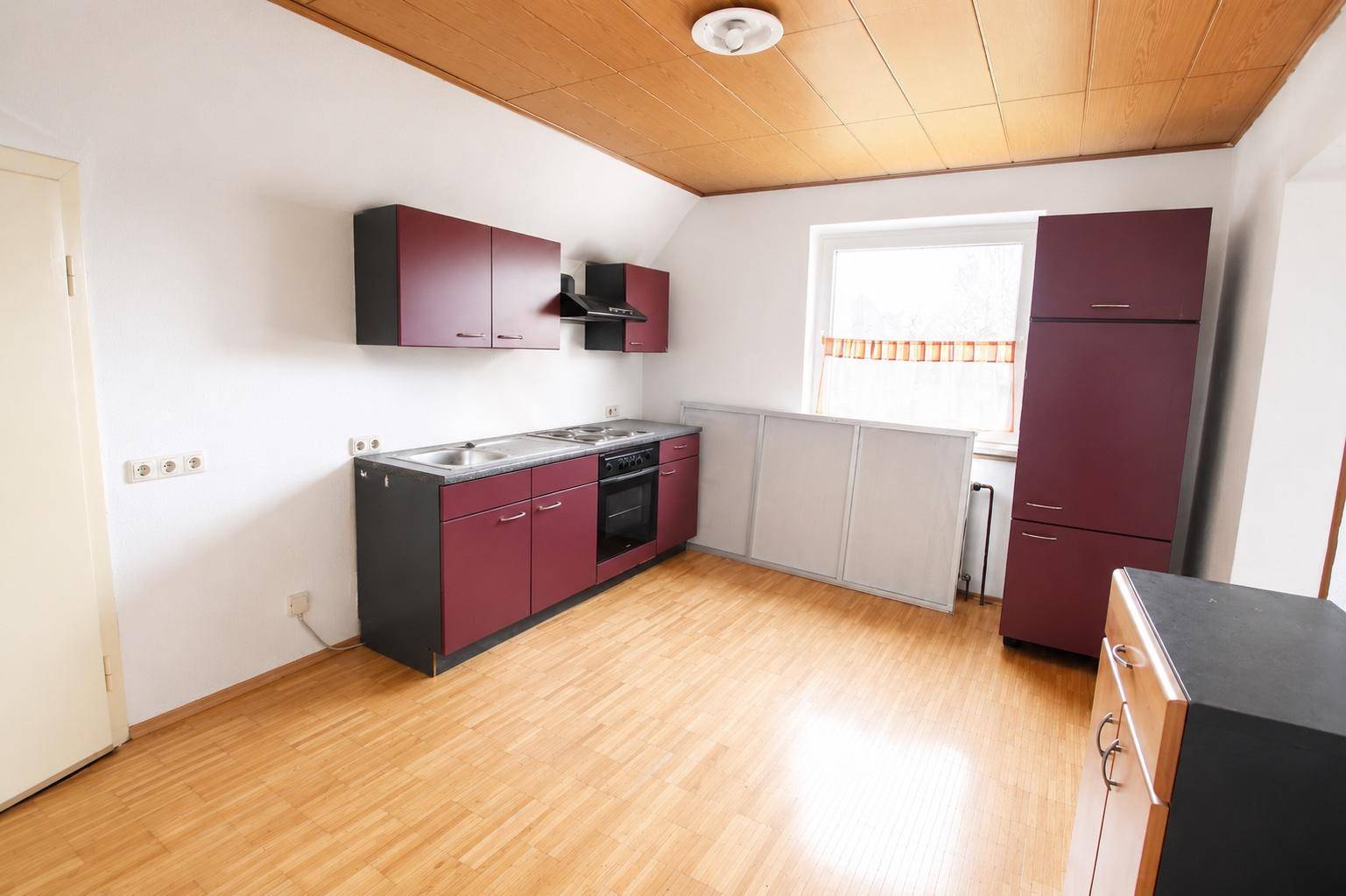 Funktionale Küche mit burgunderroten Schränken, Holzboden und Dachschräge, inklusive Geräten.