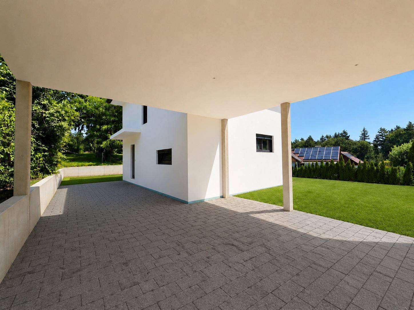 Blick vom Carport auf die Hausseite und den gepflasterten Vorplatz mit Solaranlage im Hintergrund.