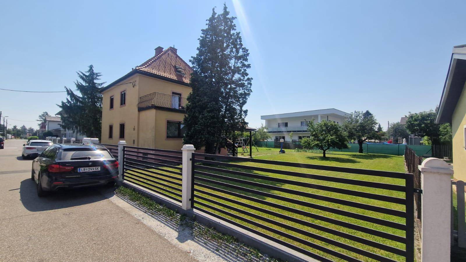 Blick auf das gelbe Wohnhaus von der Straße mit einem gepflegten Vorgarten und Zaun.