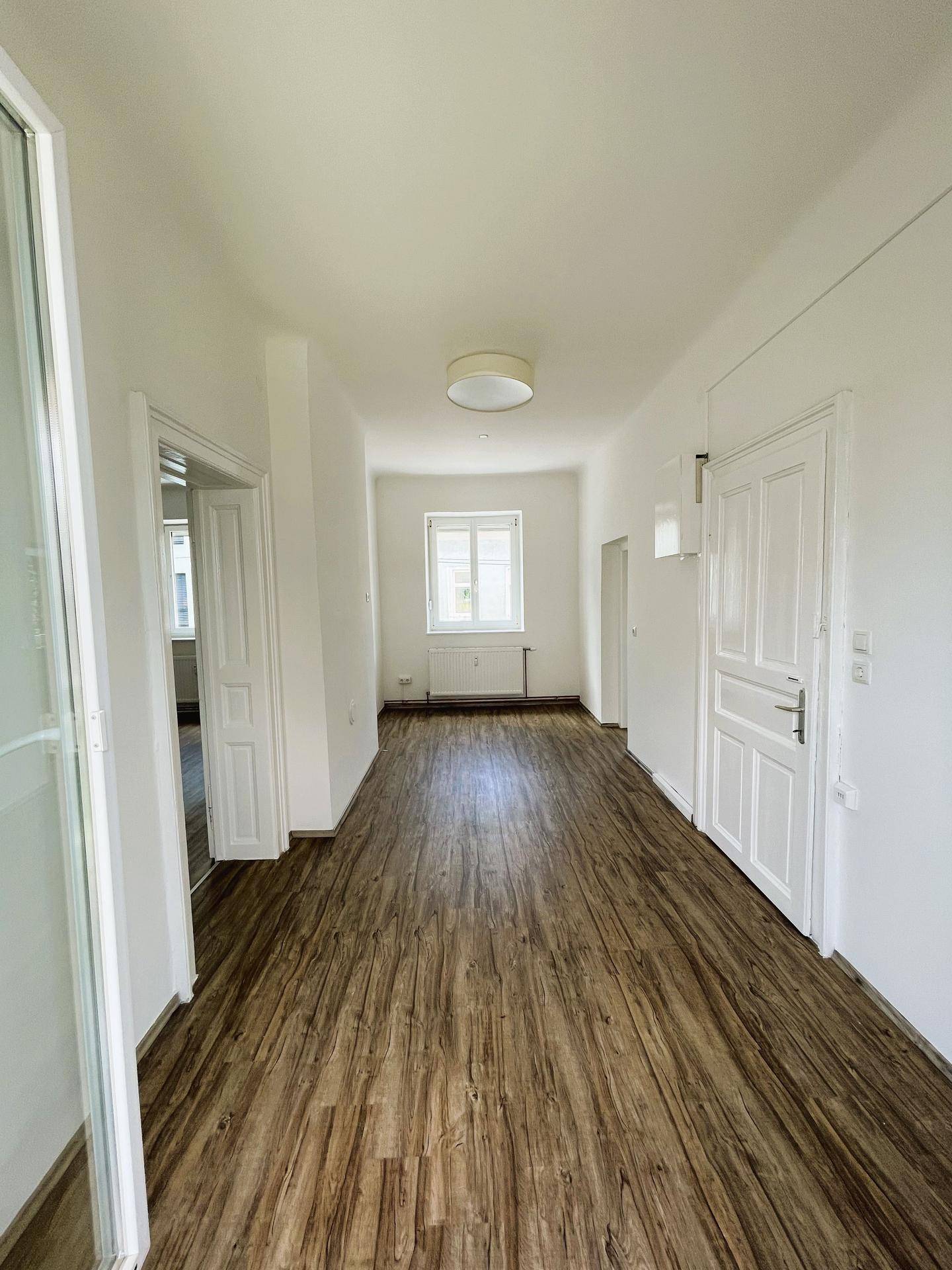 Langer, heller Flur mit Laminatboden und Fenstern, der verschiedene Räume der Wohnung verbindet.