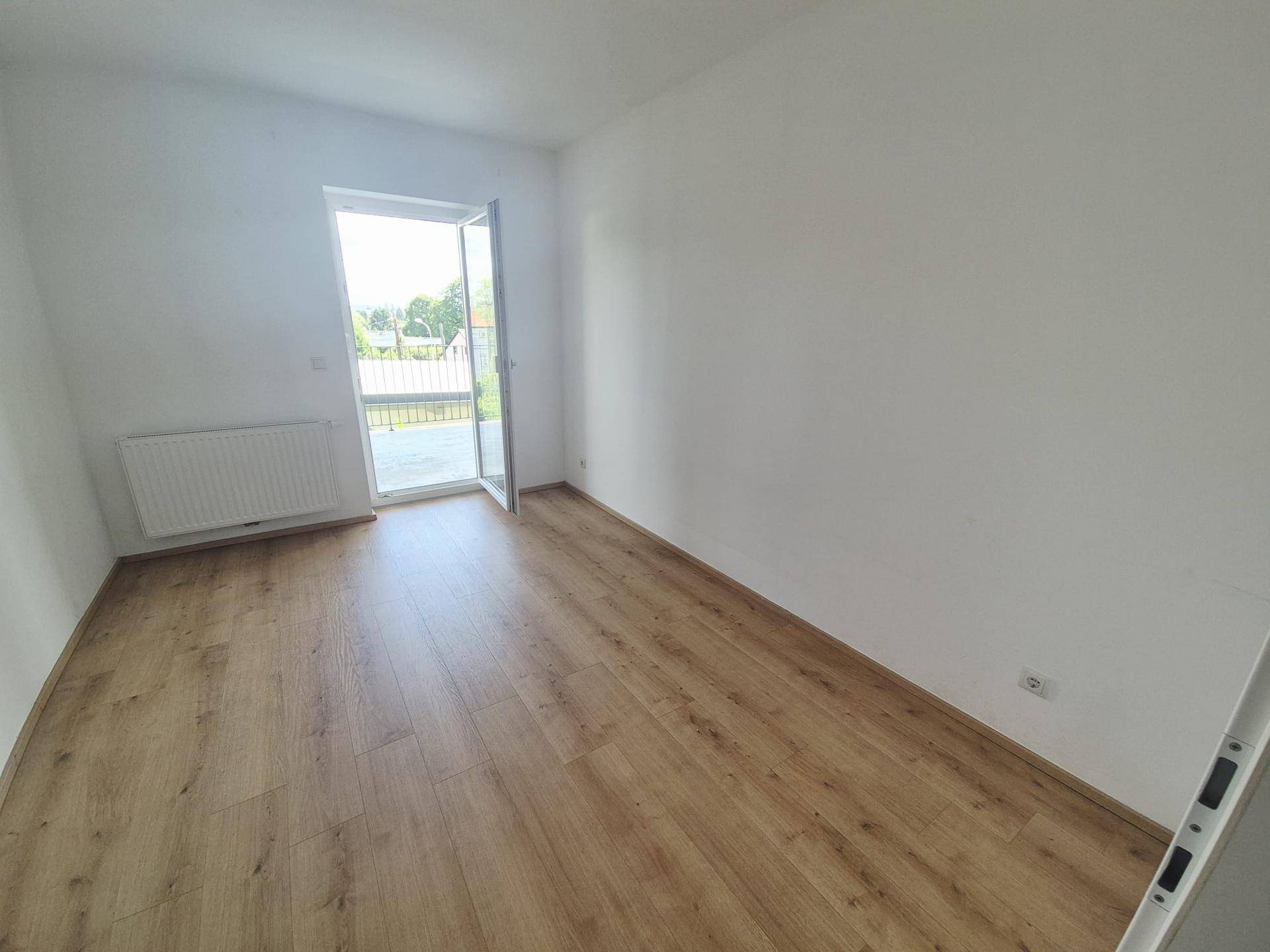 Helles Zimmer mit Laminatboden und Zugang zu einem Außenbereich, ideal als Schlaf- oder Wohnraum.
