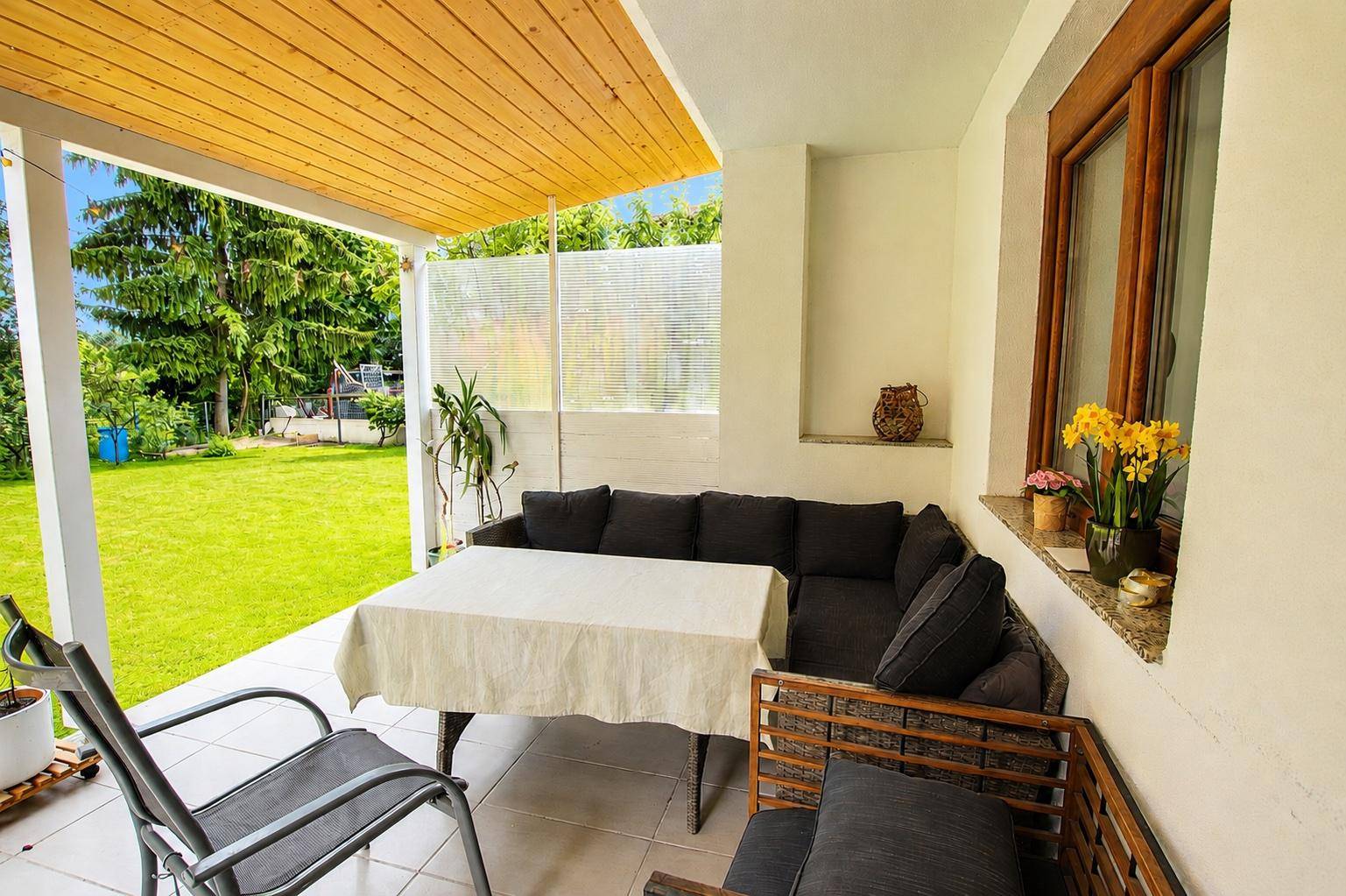 Überdachte Terrasse mit bequemen Gartenmöbeln und Blick auf den grünen Garten.