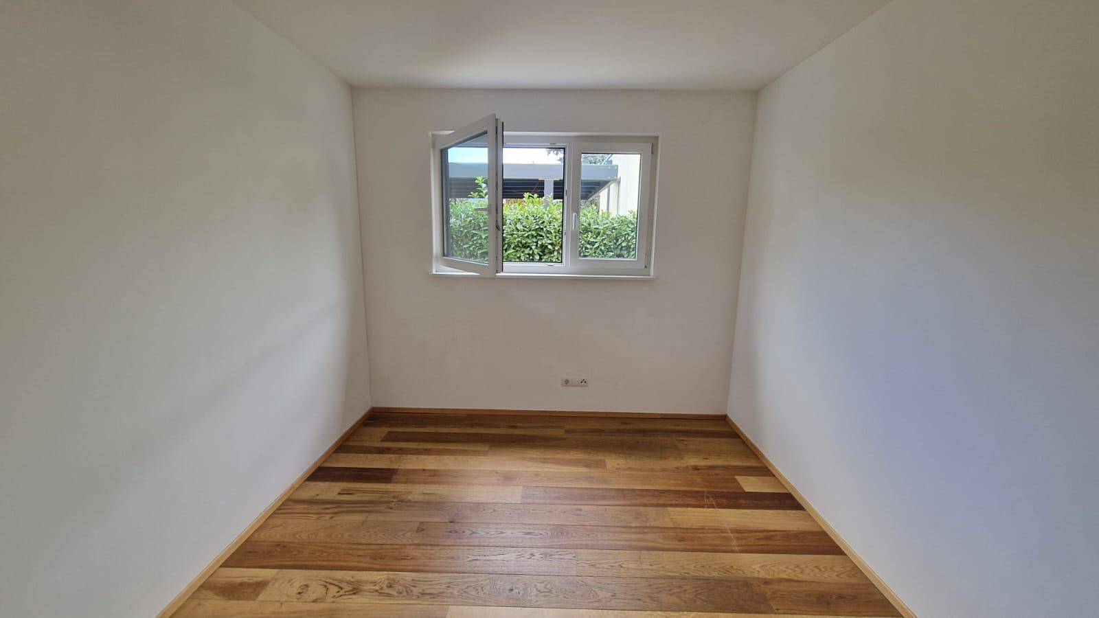 Helles Schlafzimmer mit Holzboden und Fenster mit Blick ins Grüne.