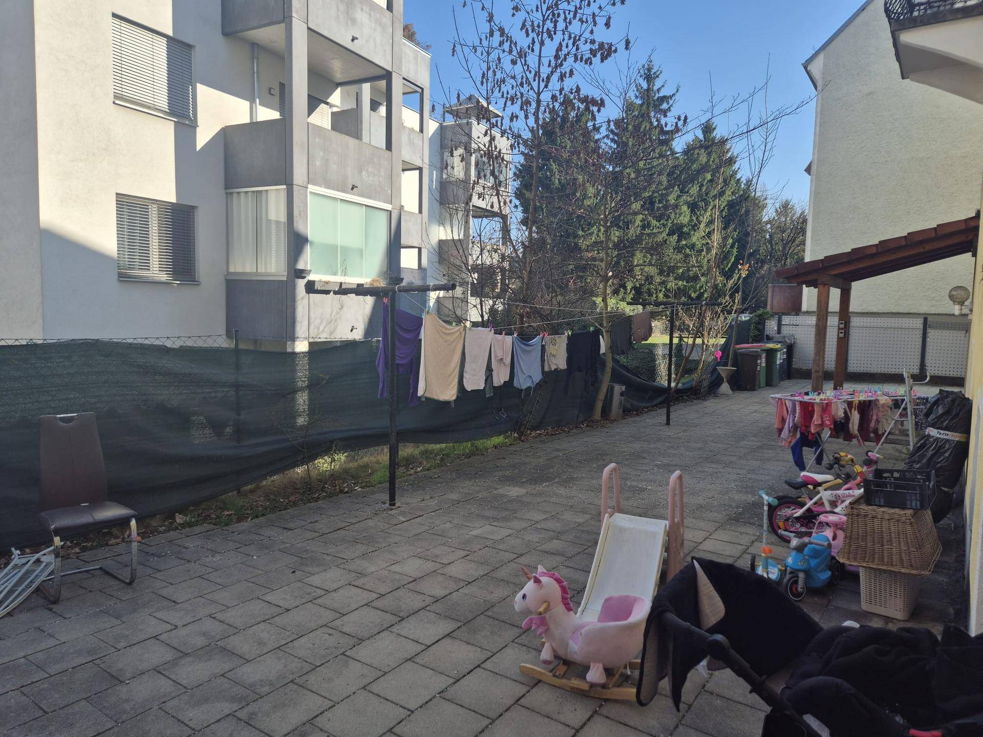 Gepflasterter Innenhof mit Kinderspielzeug und Wäscheleinen, umgeben von Wohngebäuden.