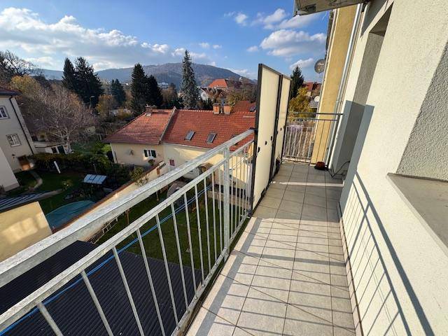 Sonniger Balkon mit Fliesenboden und weitem Blick über Dächer und grüne Hügel.