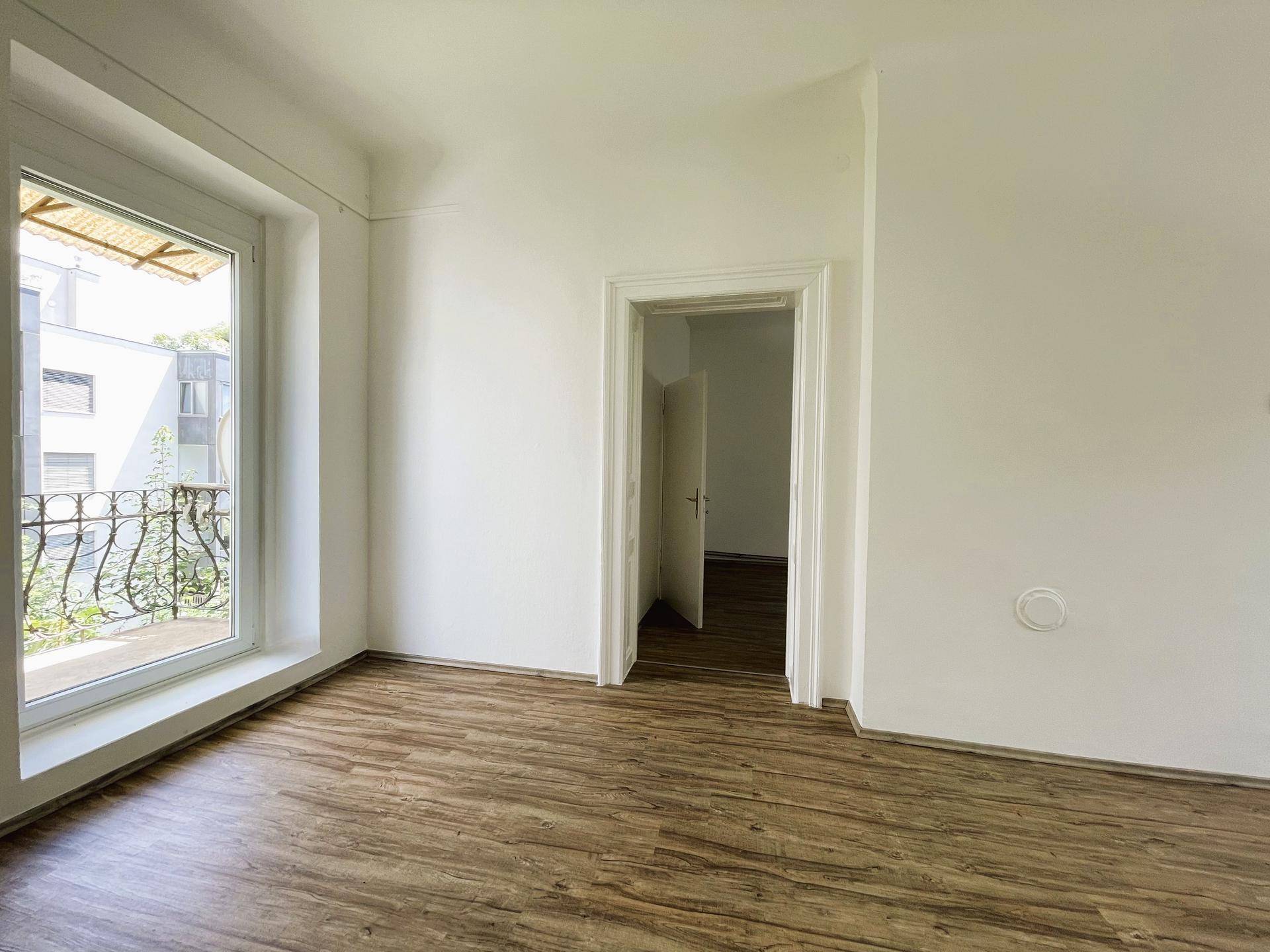Helles Zimmer mit Laminatboden und Zugang zu einem französischen Balkon, ideal als Wohn- oder Schlafzimmer.