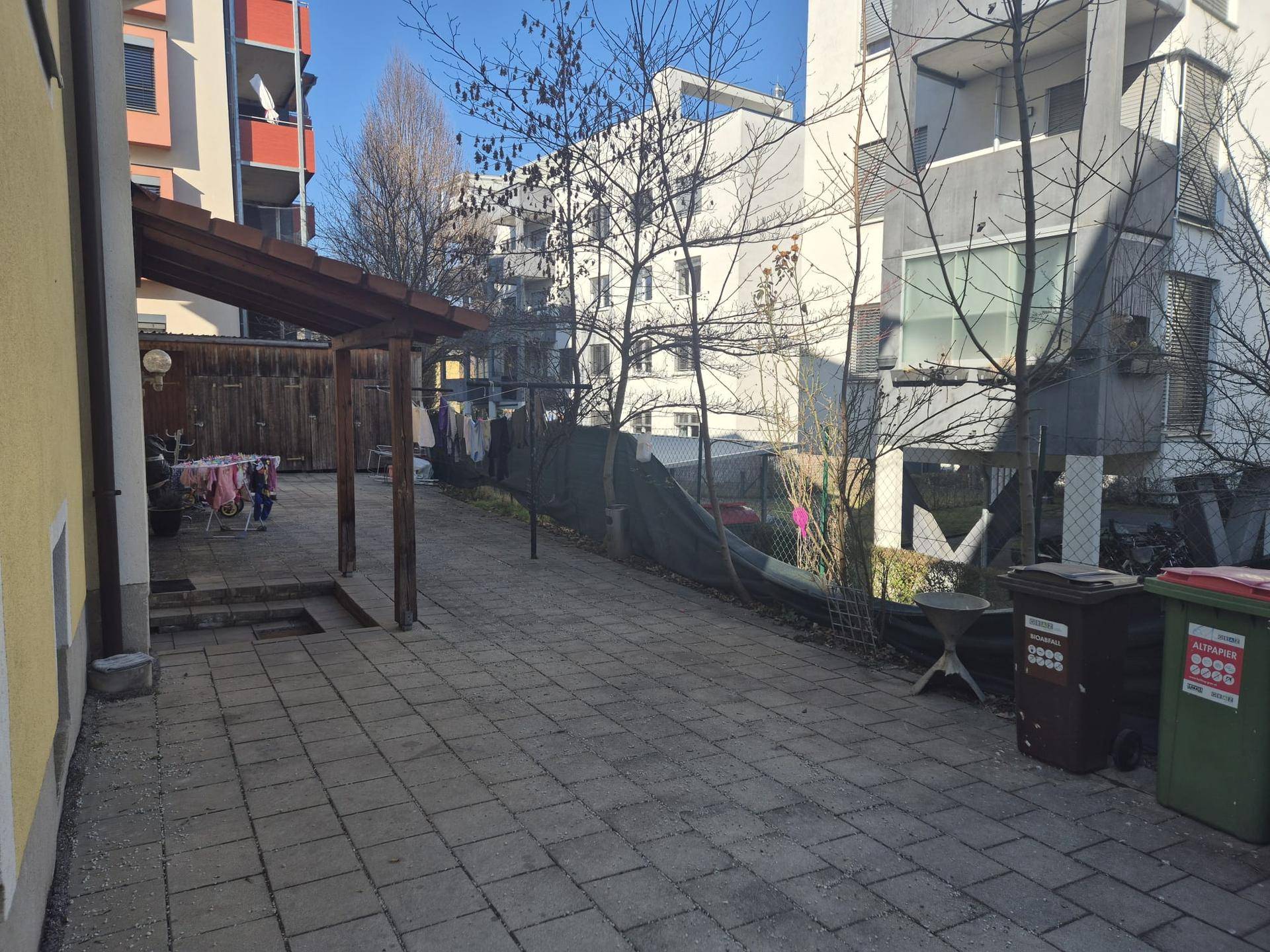 Gepflasterter Innenhof mit Holzpergola und Wäscheleinen, umgeben von Gebäuden.