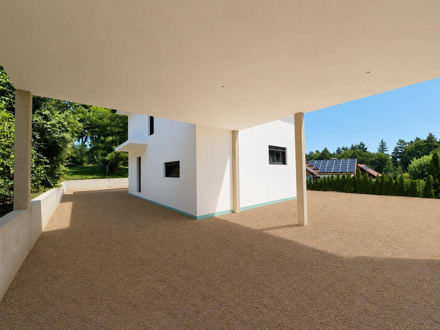 Blick vom Carport auf die Hausseite mit Kiesfläche und Solaranlage im Hintergrund.