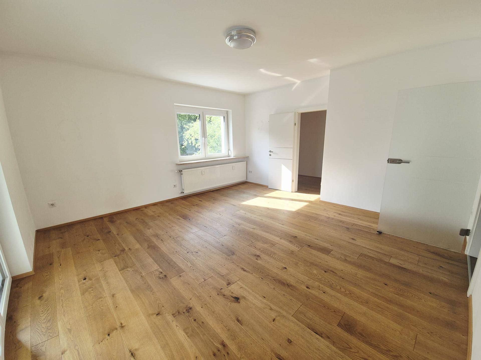 Lichtdurchflutetes Schlafzimmer mit hochwertigem Parkettboden und weiß gestrichenen Wänden.