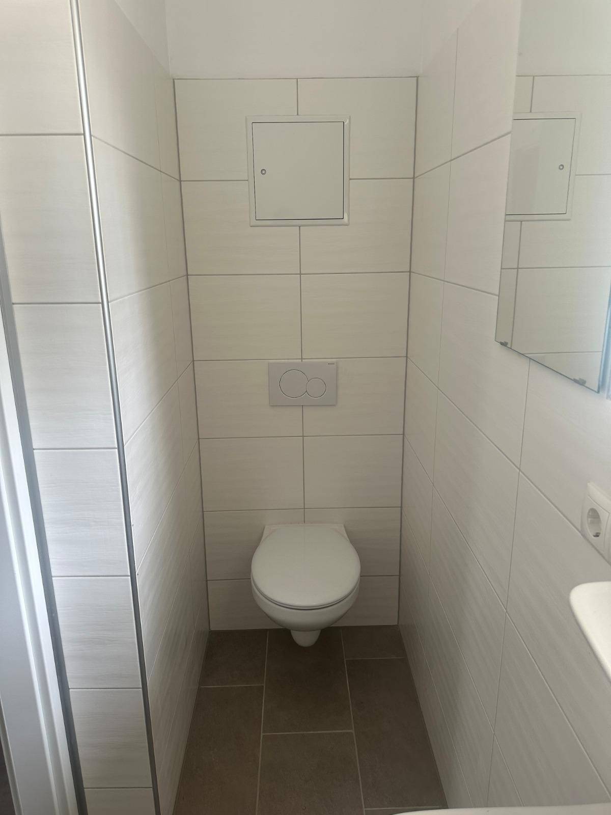 Modern gefliestes WC mit wandhängender Toilette und Spiegel an der Wand.
