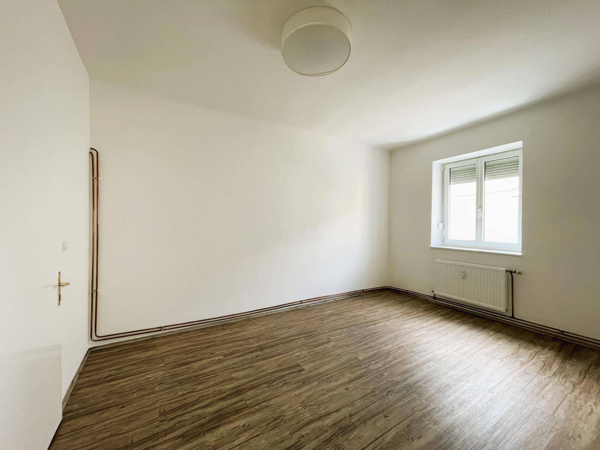 Leeres, helles Zimmer mit Laminatboden und einem Fenster, das viel natürliches Licht spendet.