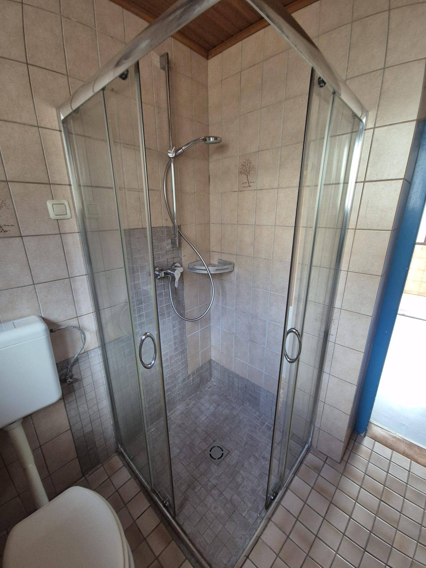 Eckduschkabine mit Glastüren und Fliesenboden im Badezimmer.