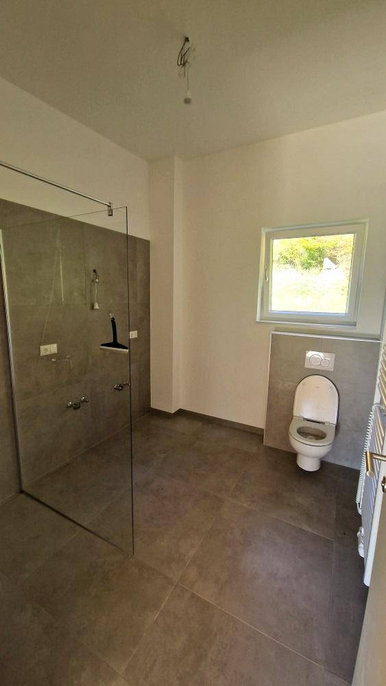 Modernes Badezimmer mit ebenerdiger Dusche, wandhängender Toilette und Fenster für Tageslicht.