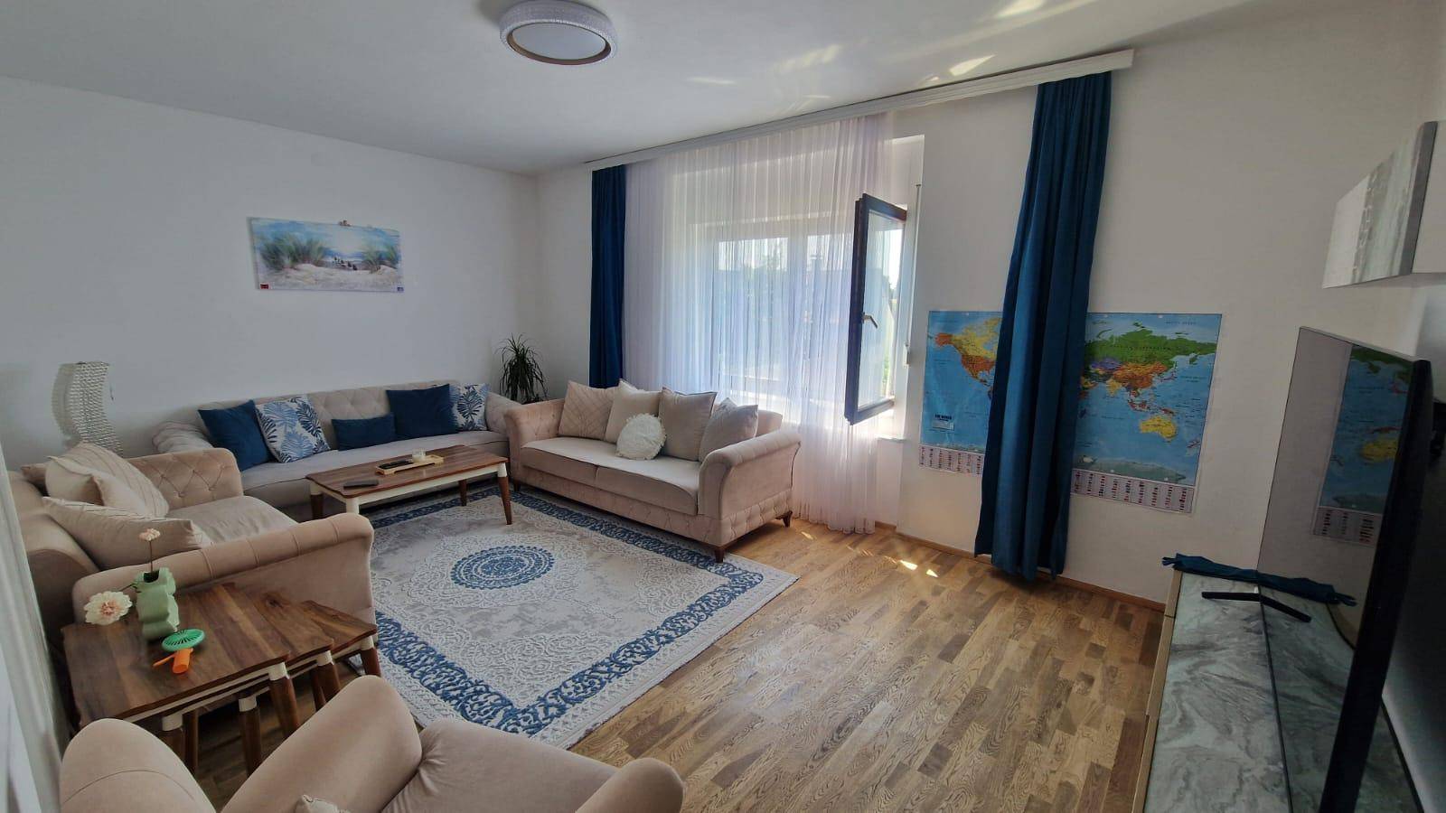 Gemütliches Wohnzimmer mit zwei Sofas, Couchtisch und Teppich, hell durch große Fenster.