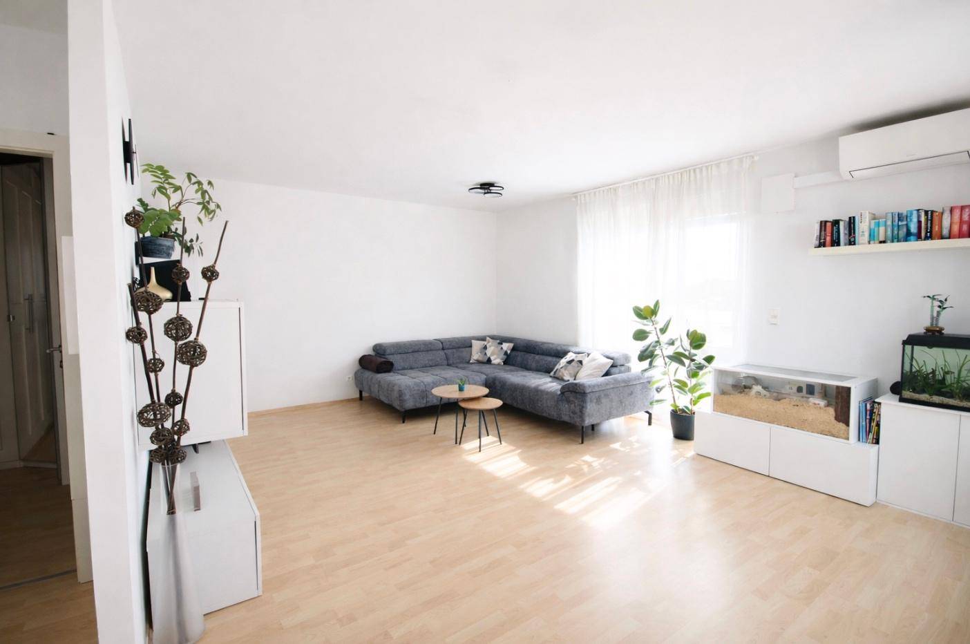 Geräumiges Wohnzimmer mit bequemer Eckcouch, hellem Holzboden und großen Fenstern.