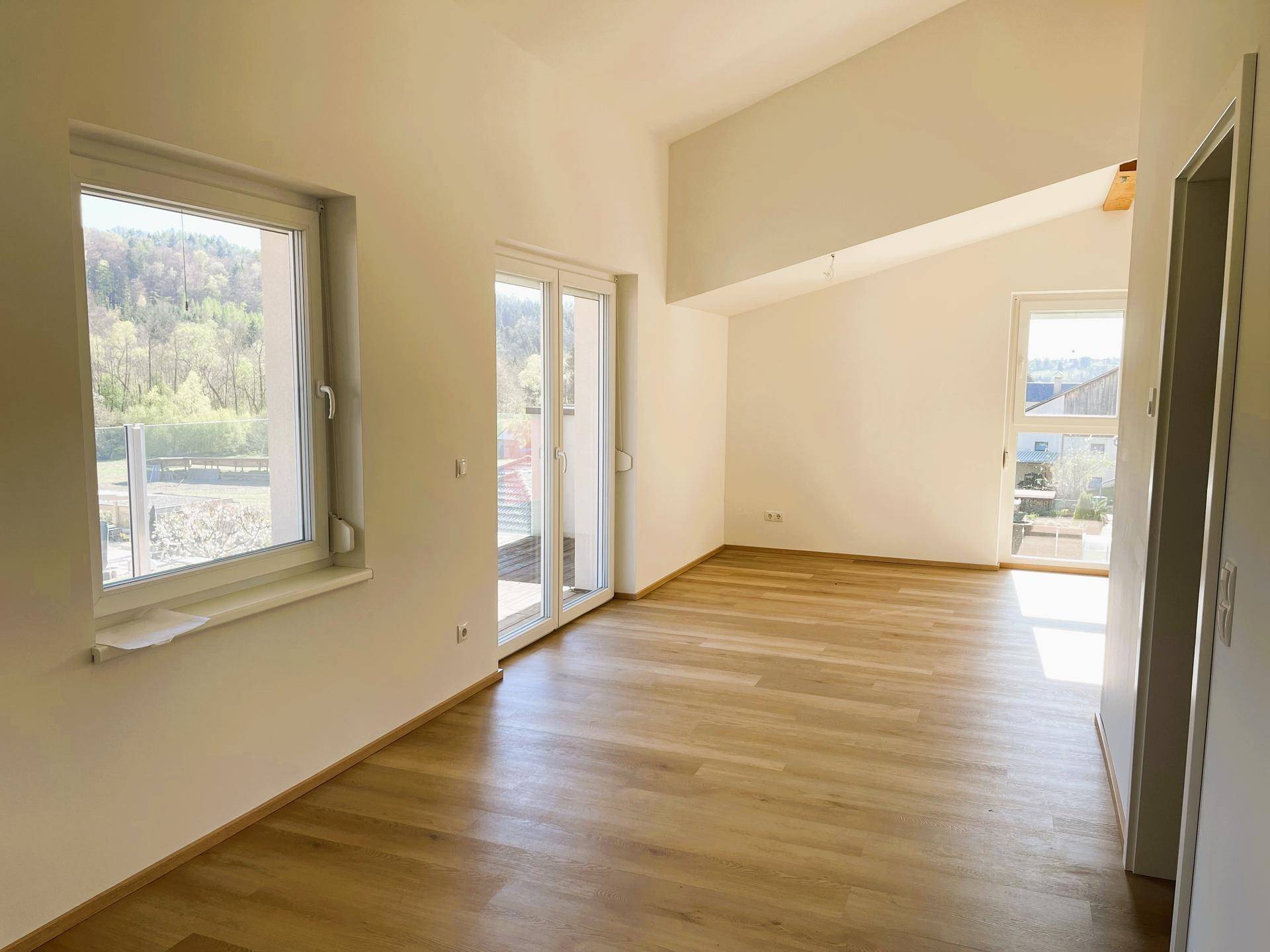 Geräumiges Wohnzimmer mit Holzboden, großen Fenstern und Zugang zu einem Außenbereich.