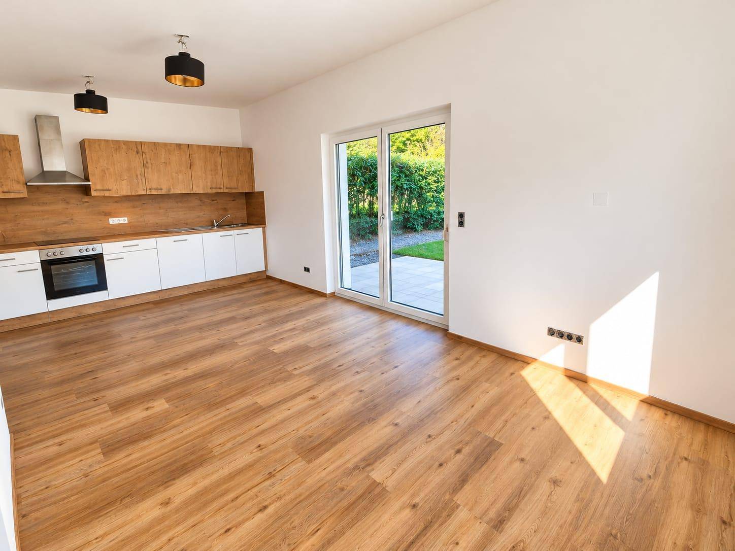 Offener Wohnbereich mit integrierter Küche und Zugang zur Terrasse durch eine große Glastür.
