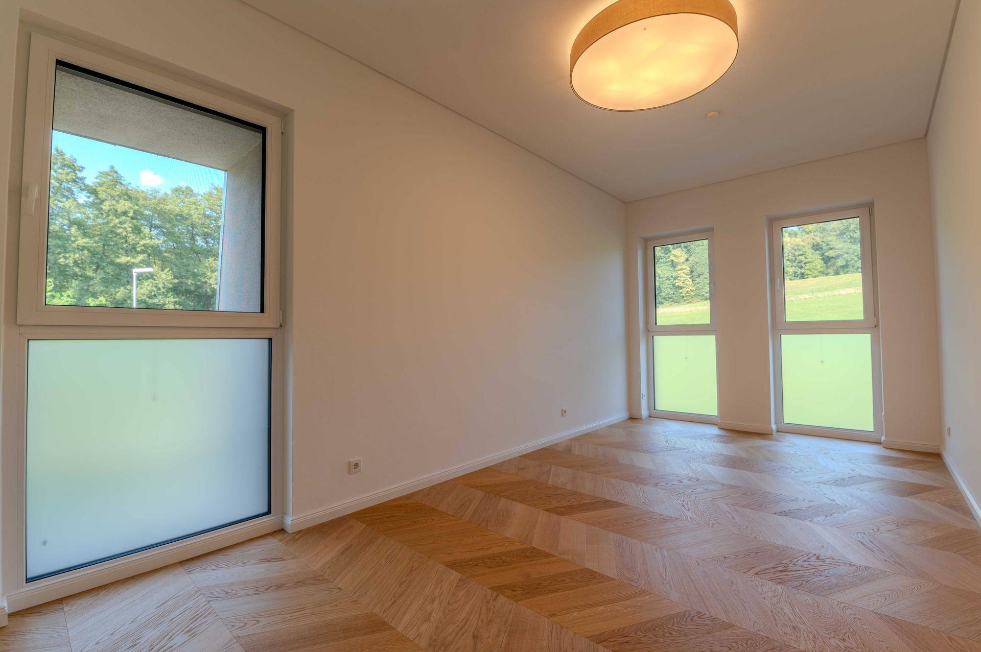 Helles Schlafzimmer mit Fischgrätparkett und großen Fenstern mit Blick ins Grüne.