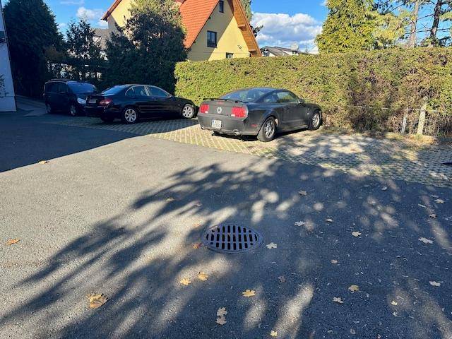 Außenparkplatz mit geparkten Autos und einer grünen Hecke im Hintergrund.