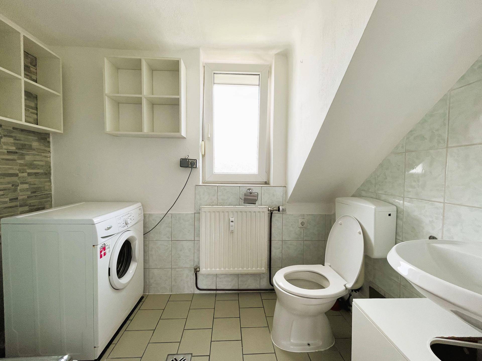 Helles Badezimmer mit WC, Waschbecken, Waschmaschine und Fenster unter einer Dachschräge.