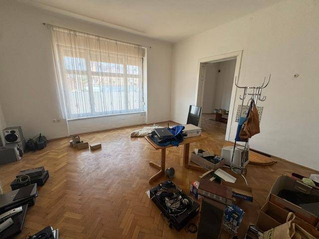 Geräumiges Wohnzimmer mit Fischgrätparkett und einem großen Fenster, das viel Tageslicht hereinlässt.
