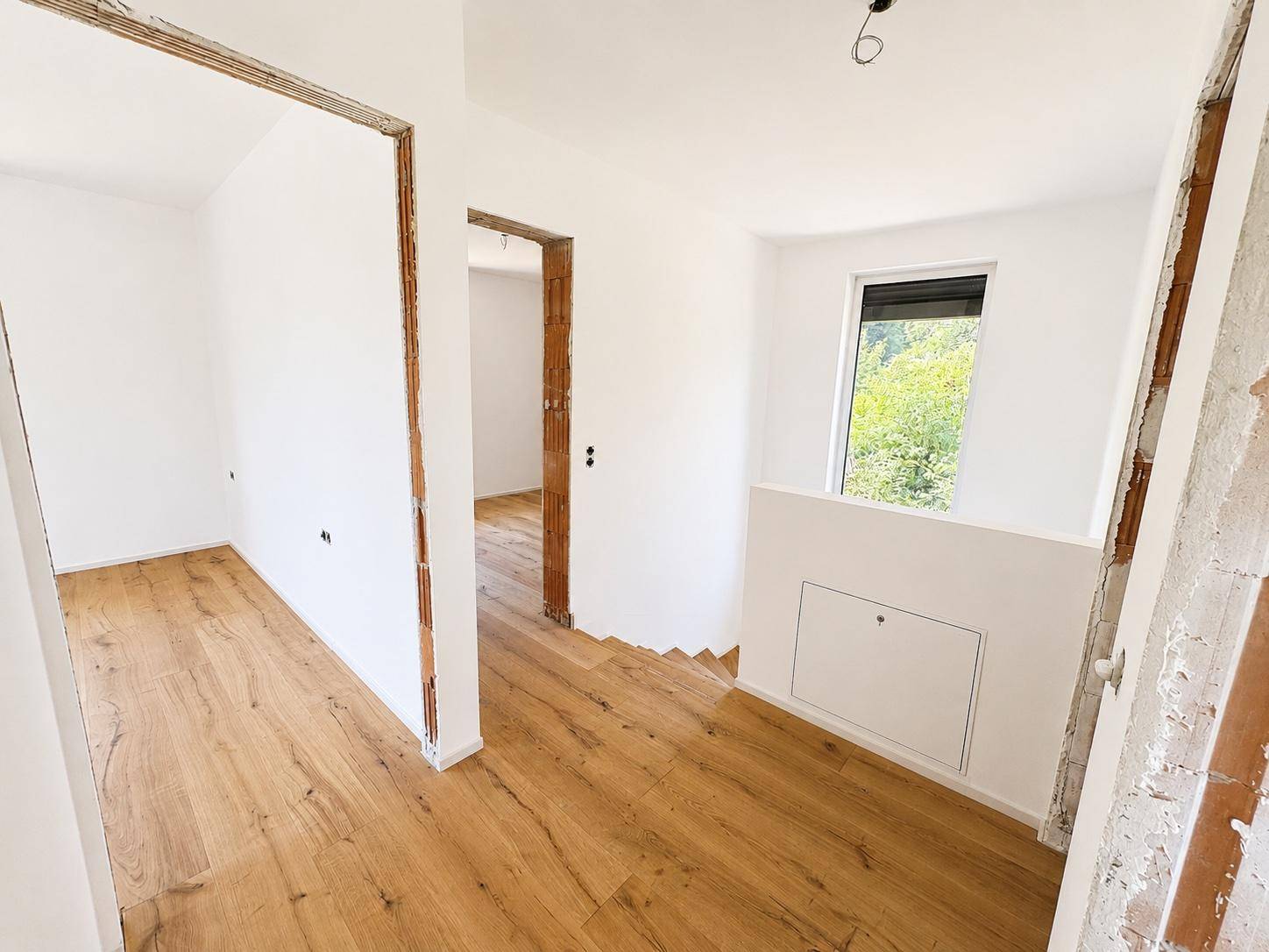 Heller Flur mit Holzparkett, einem Fenster und Zugang zu weiteren Räumen sowie einer Treppe.