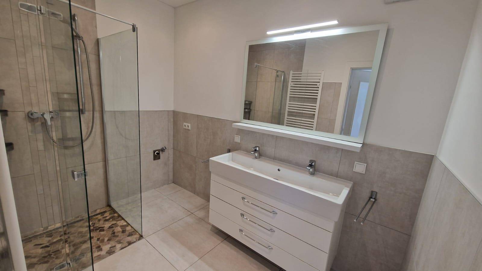 Modernes Badezimmer mit Doppelwaschbecken, großer Dusche und beheiztem Handtuchhalter.