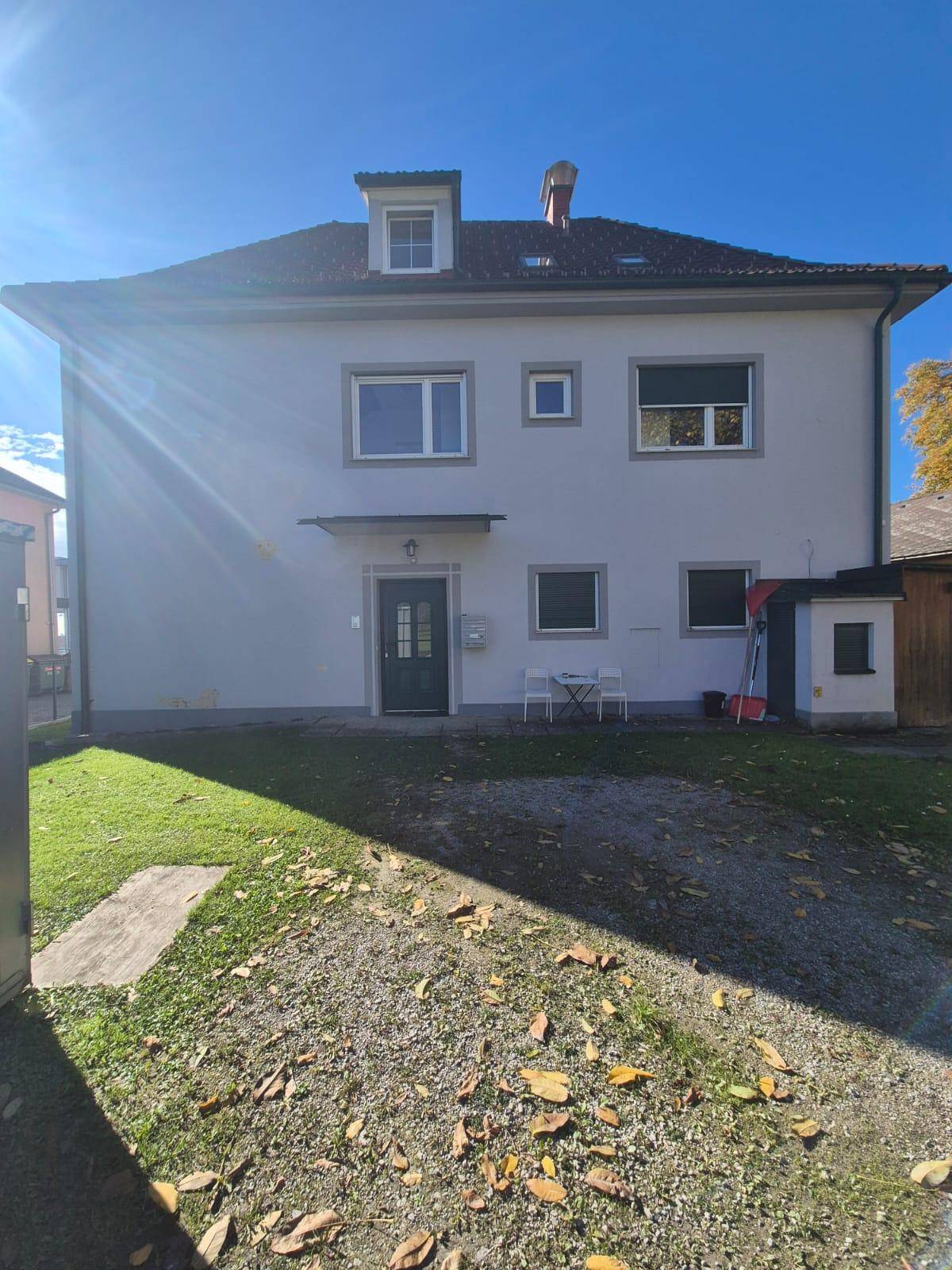 Rückansicht des Gebäudes mit grünem Rasen, Kiesweg und kleiner Terrasse im Freien.
