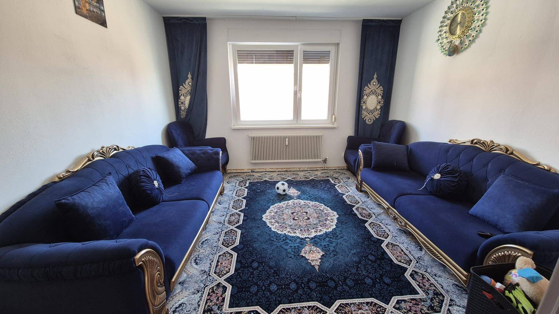 Gemütliches Wohnzimmer mit zwei großen blauen Samtsofas und einem passenden Teppich.