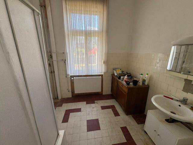 Badezimmer mit Duschkabine, Waschbecken und Fenster, ältere Fliesen im 80er-Jahre-Stil.