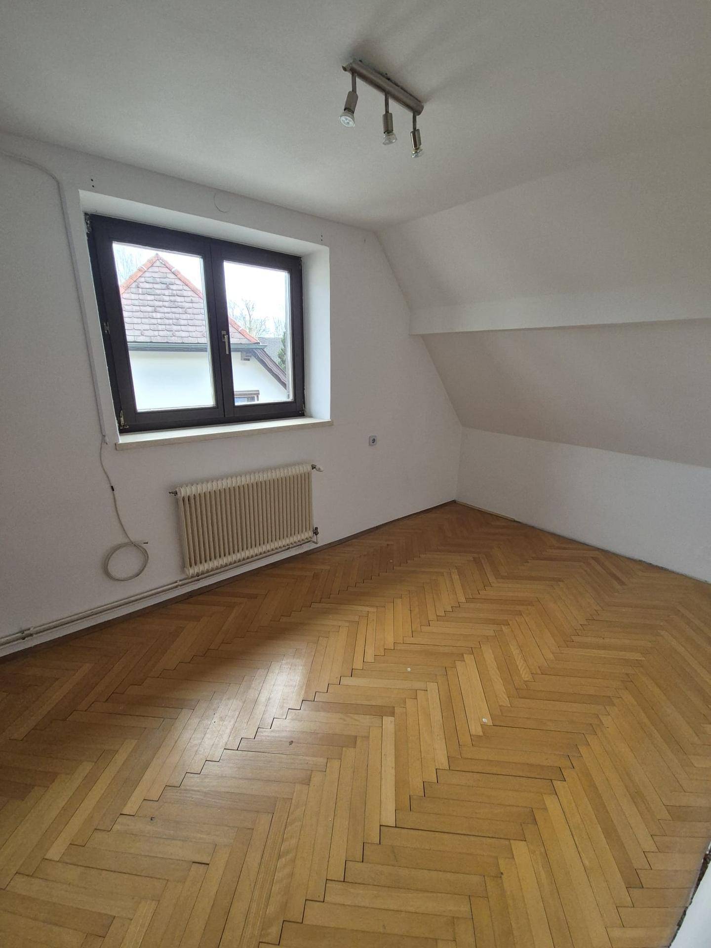 Helles Schlafzimmer im Dachgeschoss mit Fischgrätparkett und einem Fenster.