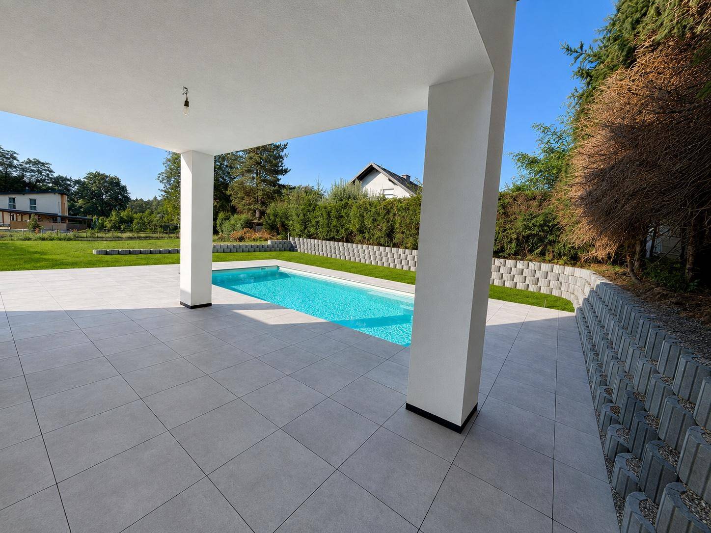 Geräumige, überdachte Terrasse mit Blick auf den Pool und die umgebende Grünfläche.
