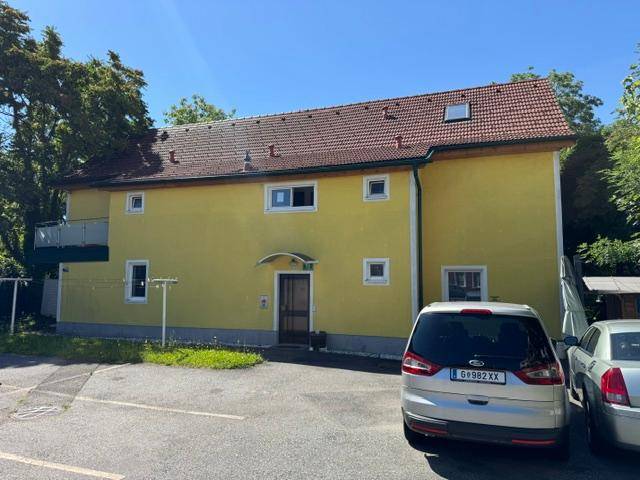 Gelbes Wohngebäude mit rotem Ziegeldach, kleinen Fenstern und einem Balkon an der Seite des Hauses.