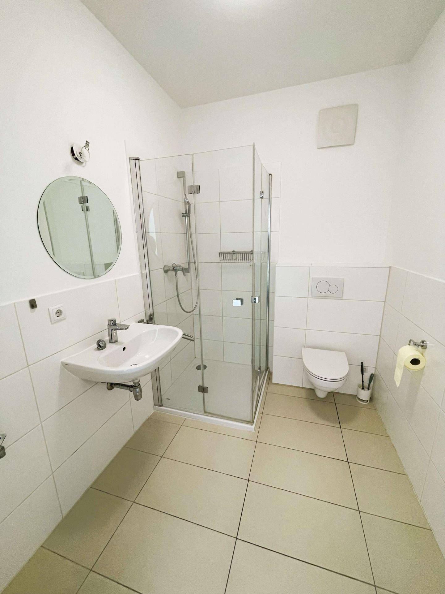 Modernes Badezimmer mit Duschkabine, WC und Waschbecken, hell gefliest.