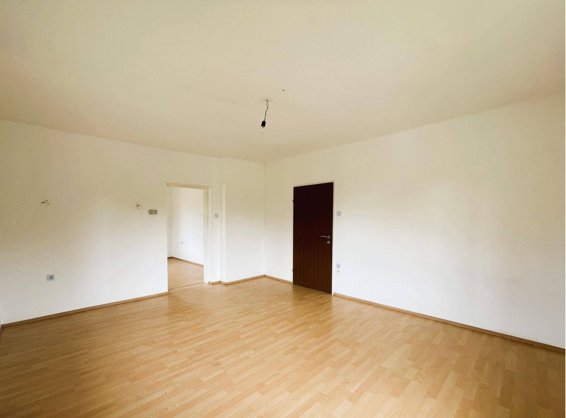 Geräumiger, leerer Raum mit hellem Laminatboden und weiß gestrichenen Wänden.