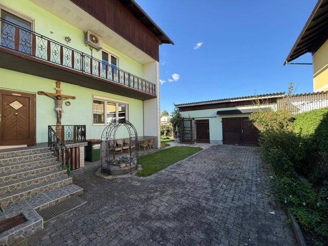 Seitenansicht des Hauses mit gepflasterter Auffahrt, Garage und einem Balkon im Obergeschoss.