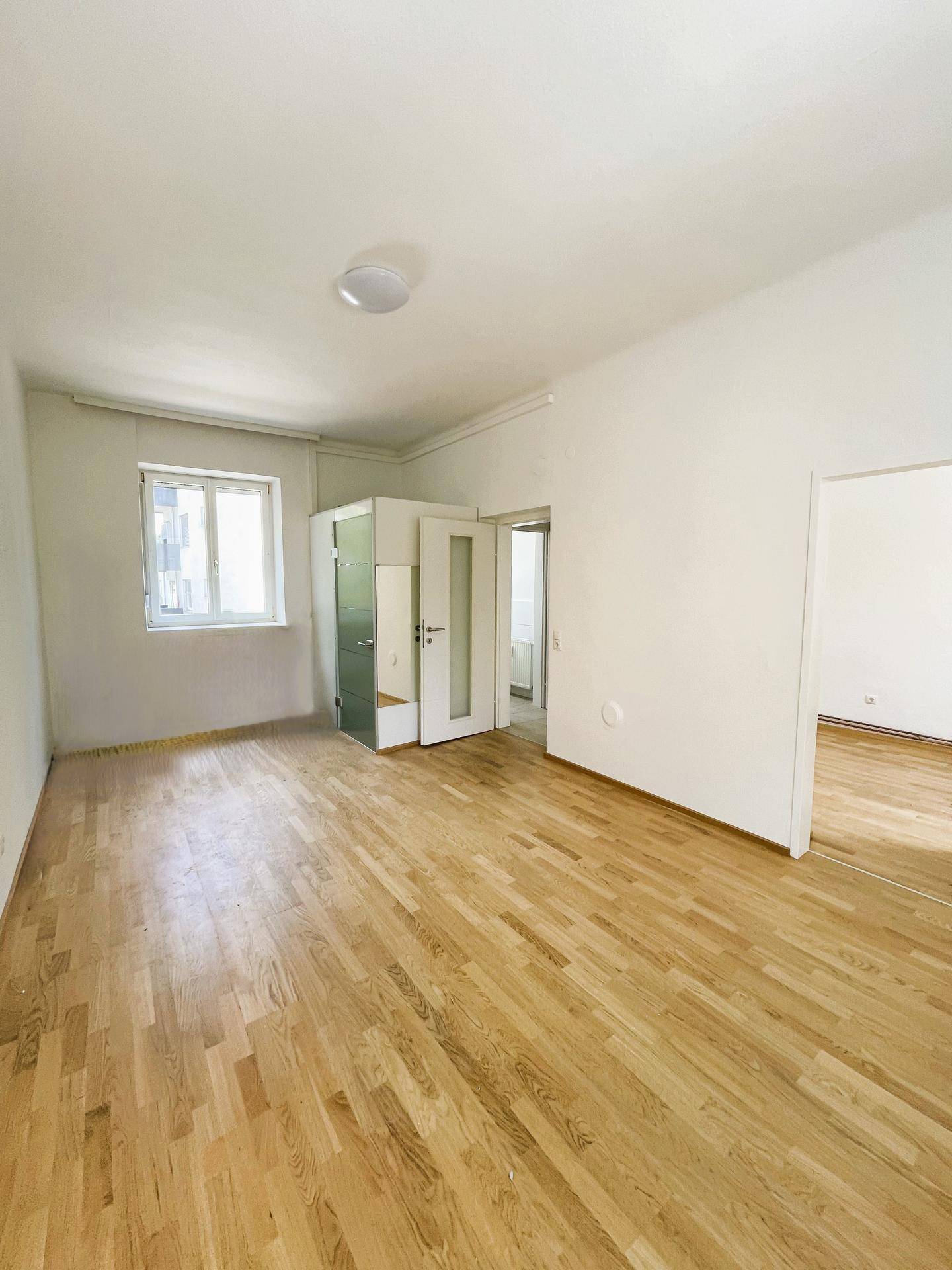 Geräumiges Zimmer mit Parkettboden, weißen Wänden und Zugang zu weiteren Räumen.