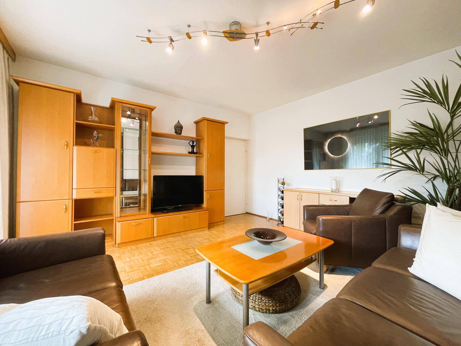 Gemütliches Wohnzimmer mit großer Holzschrankwand, Ledersofas und Parkettboden.