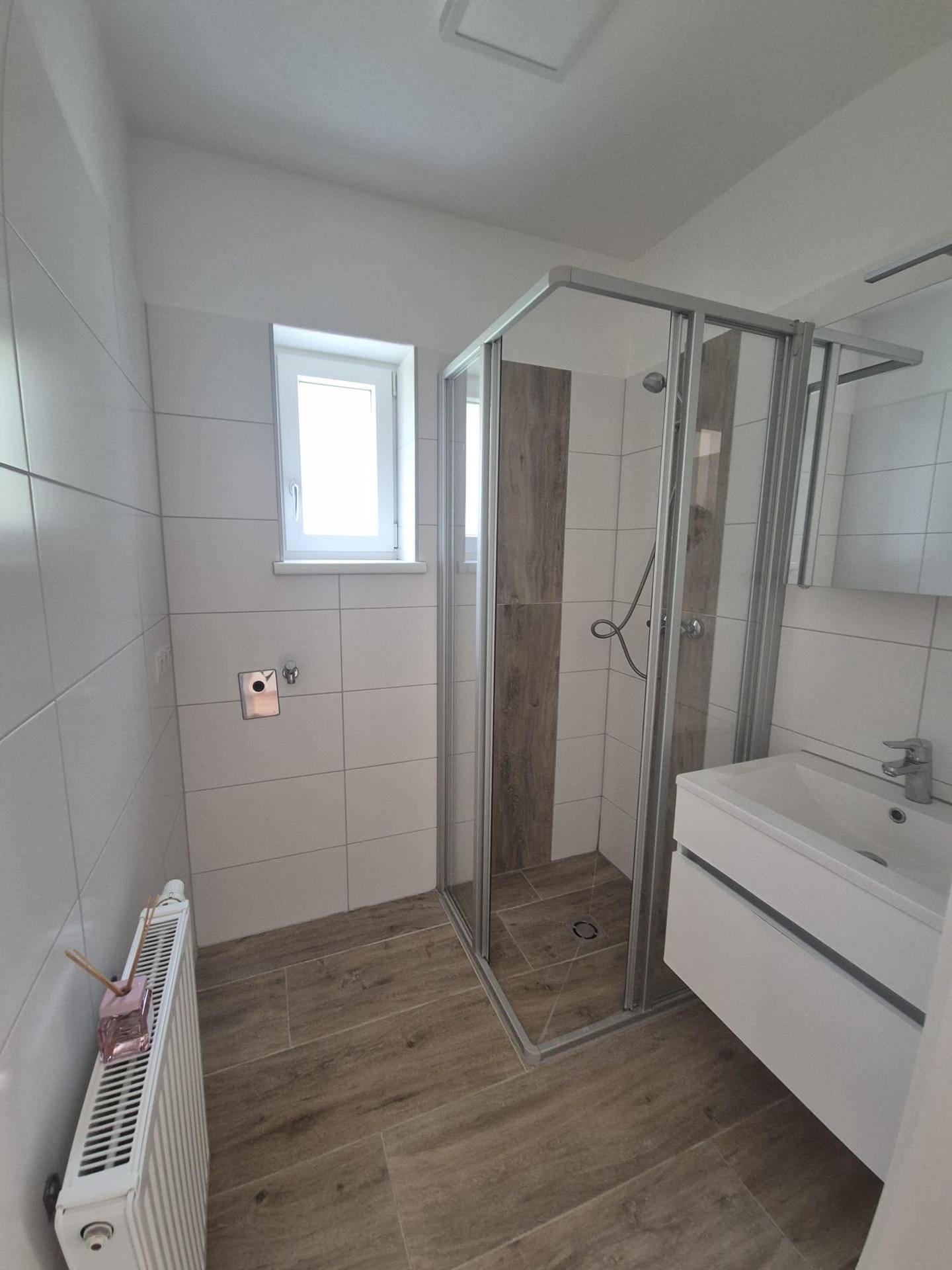 Modernes Badezimmer mit Duschkabine, Waschbecken und einem Fenster für natürliche Belüftung.
