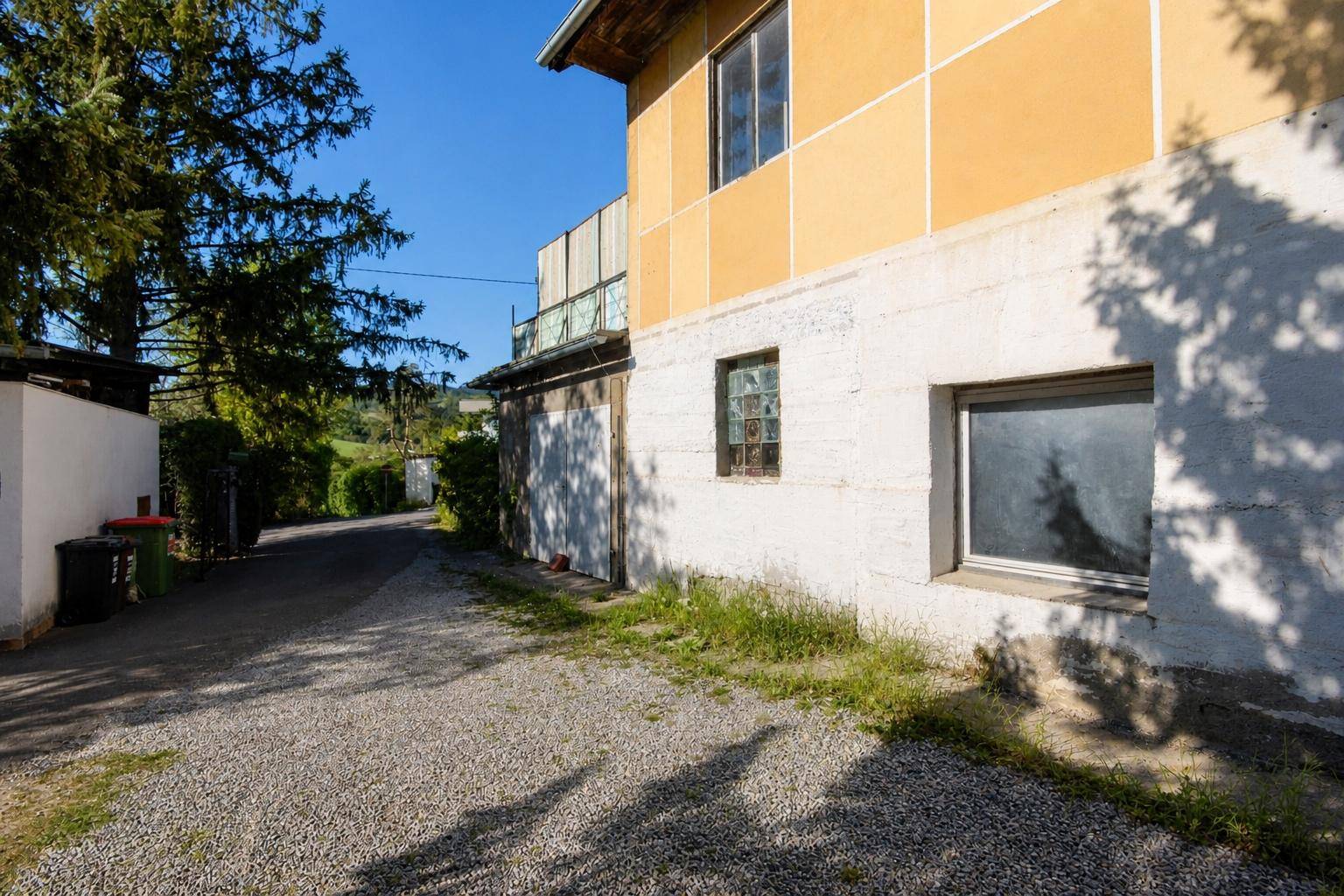 Seitenansicht eines Hauses mit gelber Fassade, weißen Wänden und Schotterweg.
