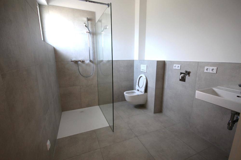 Modernes Badezimmer mit ebenerdiger Dusche, Wand-WC und Einzelwaschbecken.