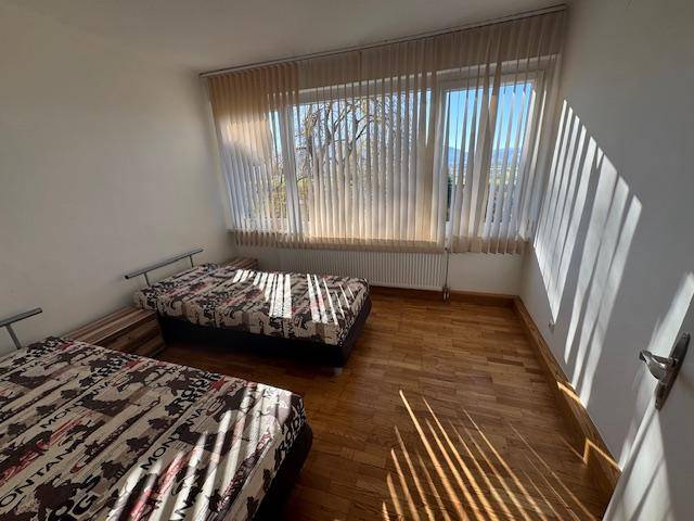 Schlafzimmer mit zwei Einzelbetten und großem Fenster, das viel Tageslicht hereinlässt.