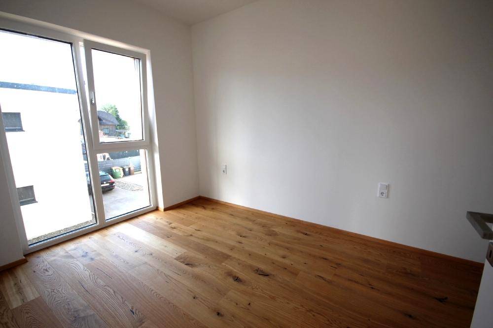 Geräumiges Schlafzimmer mit großen Fenstern, Holzboden und viel Tageslicht.