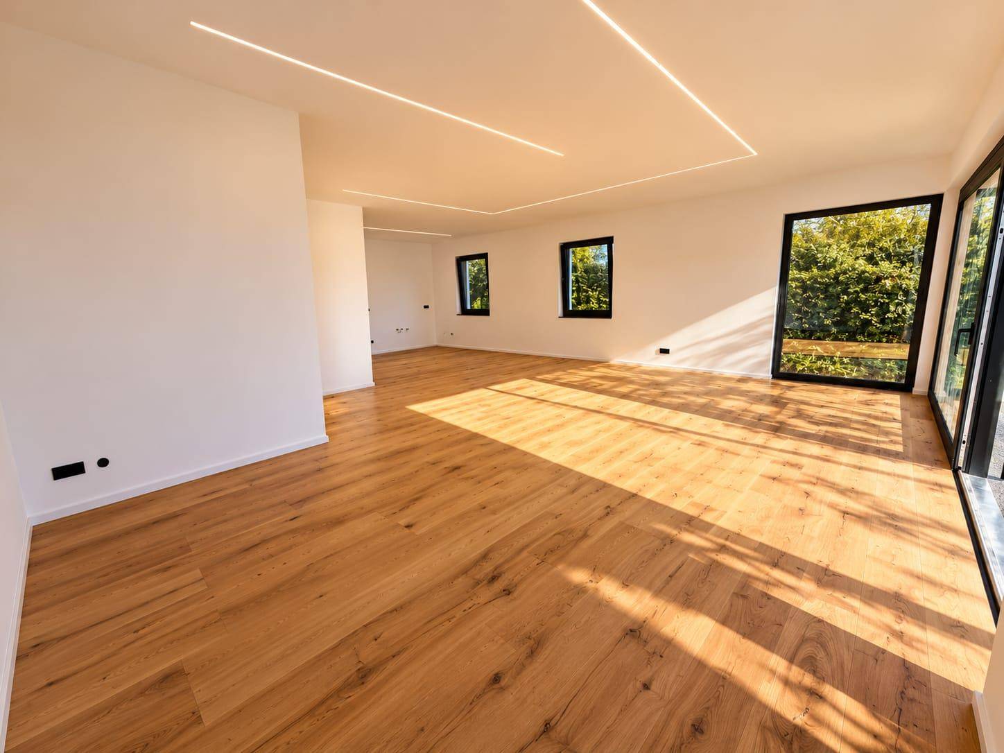 Geräumiger, heller Wohnbereich mit Holzboden und großen Fenstern, die viel Tageslicht hereinlassen.