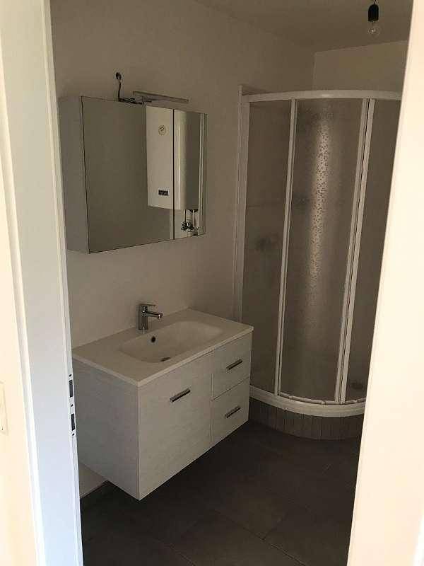 Modernes Badezimmer mit Duschkabine, Einzelwaschbecken und Spiegelschrank auf dunklem Fliesenboden.