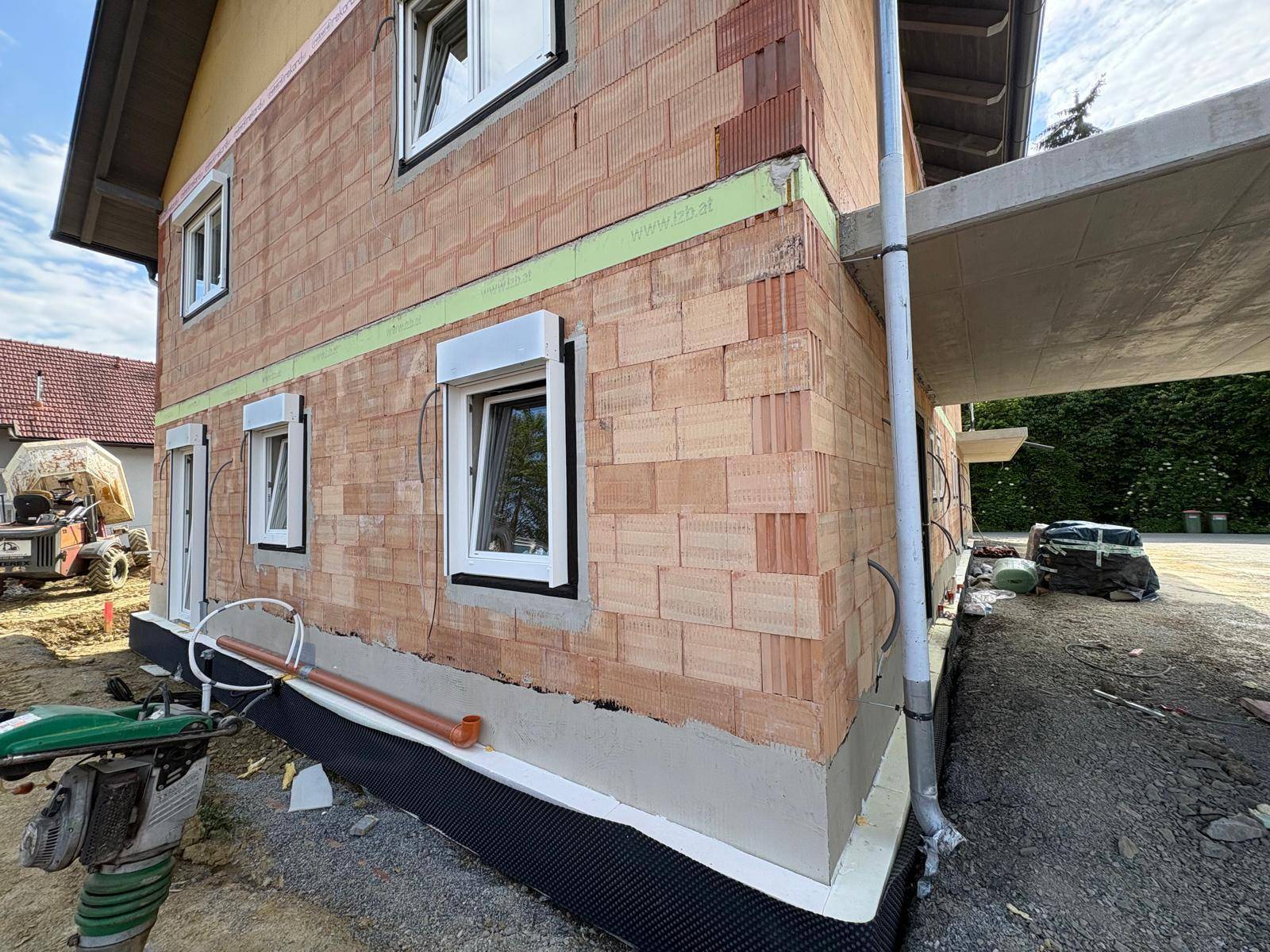 Nahaufnahme einer Hausecke im Rohbau mit Ziegelwänden, Fenster und sichtbaren Baudetails.